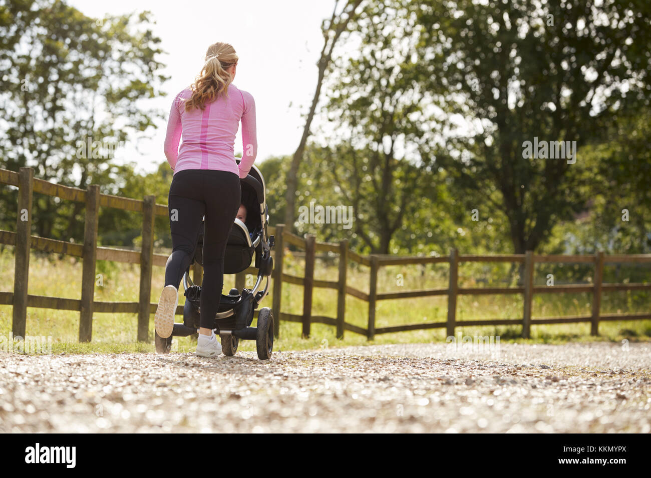 Rear View Of Mother Exercising By Running And Pushing Baby Buggy Stock Photo