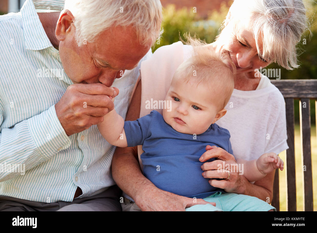 Grandparents Sitting On Seat In Garden With Baby Grandson Stock Photo