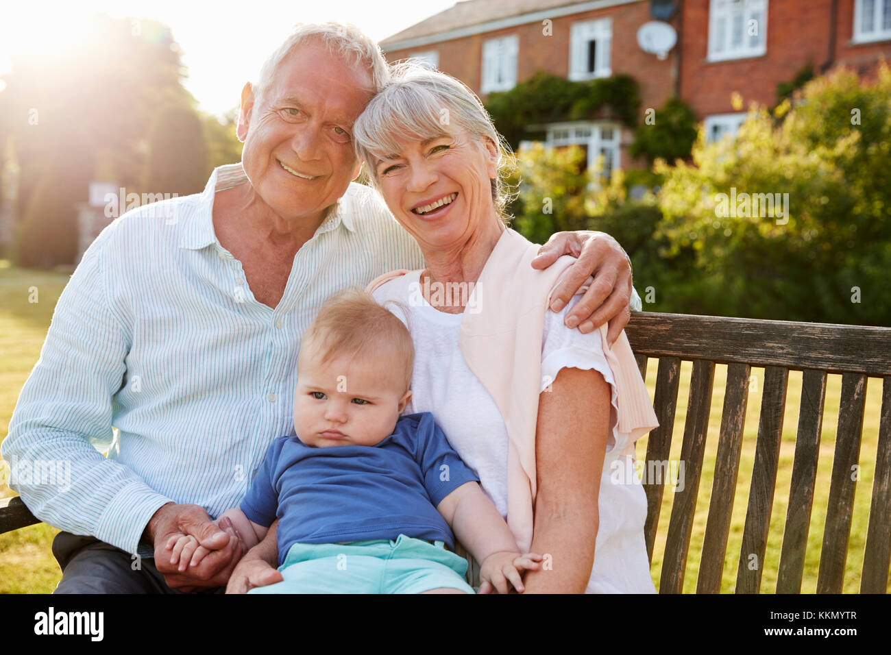 Grandparents Sitting On Seat In Garden With Baby Grandson Stock Photo