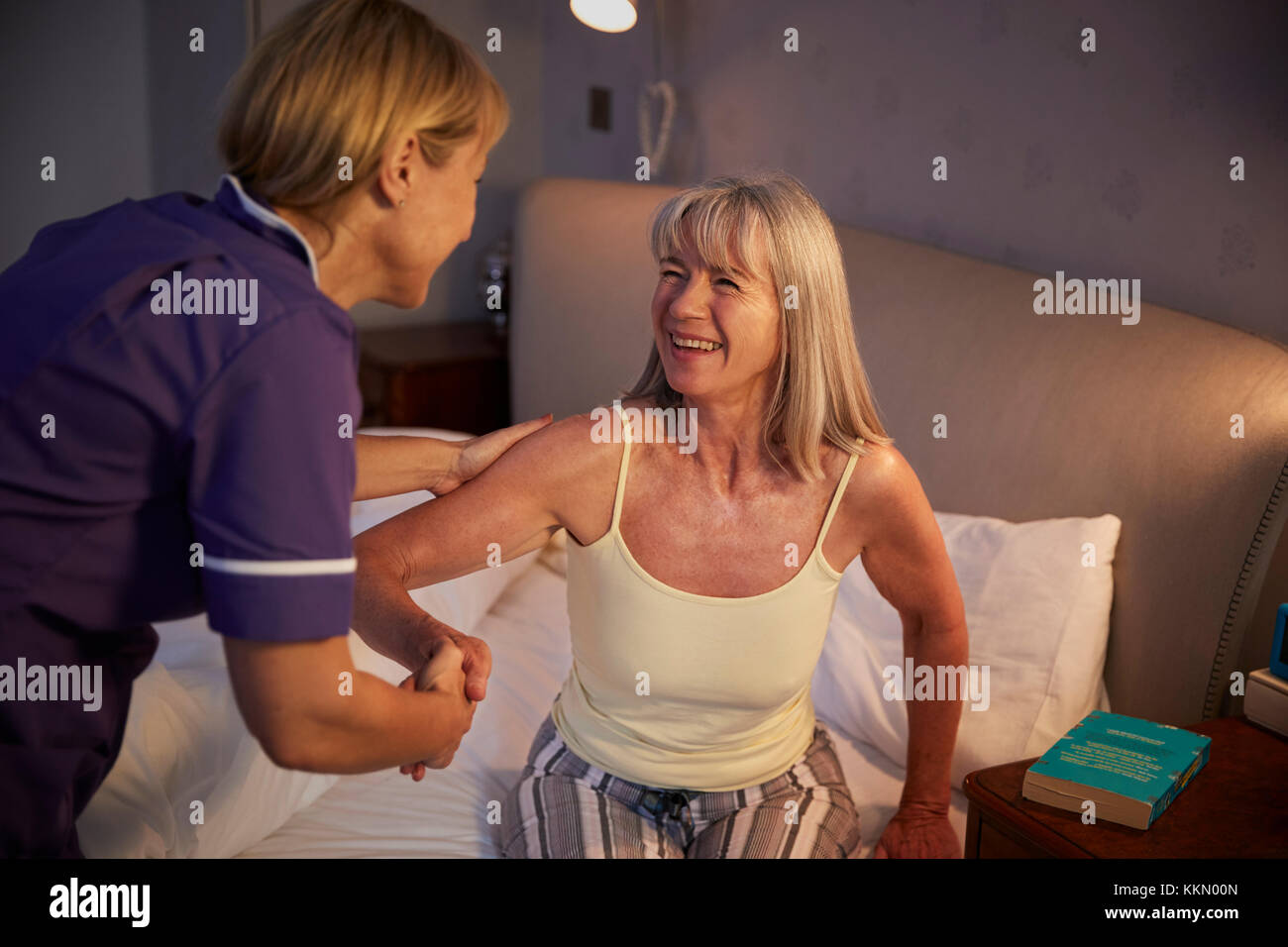 Nurse Helping Senior Woman Out Of Bed On Home Visit Stock Photo
