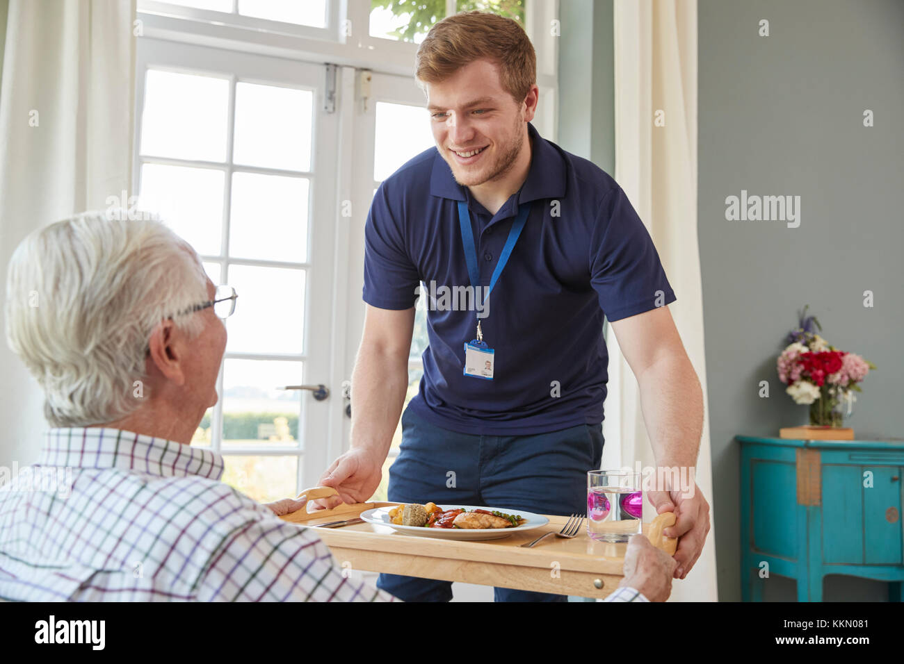 Male care worker serving dinner to a senior man at his home Stock Photo