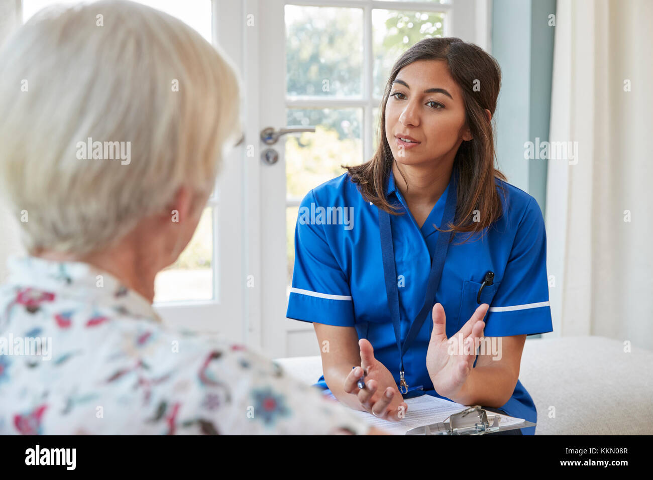 Senior woman talking to young care nurse on home visit Stock Photo