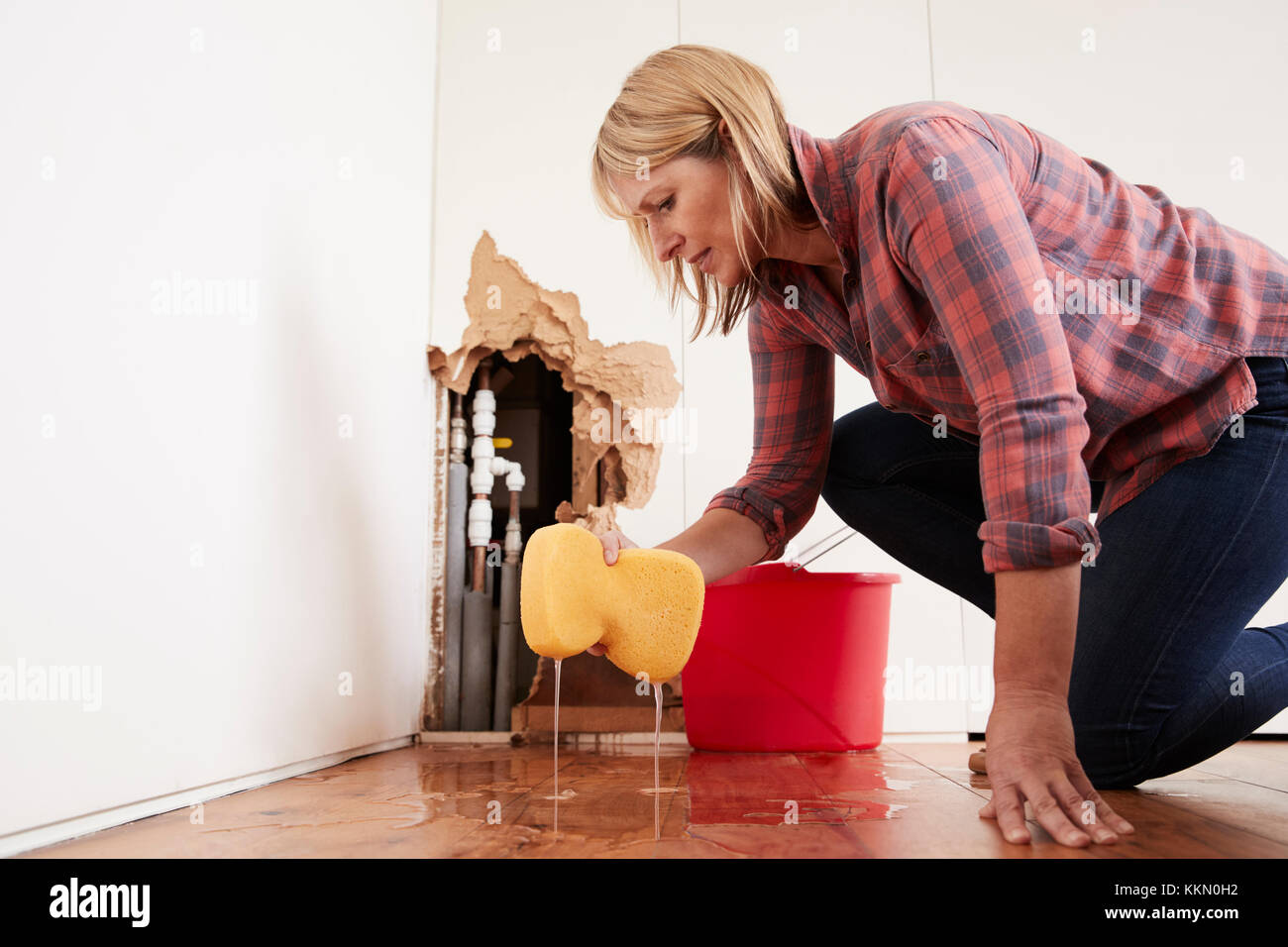 Worried woman mopping up water from a burst pipe with sponge Stock Photo