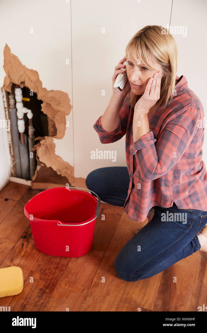 Middle aged woman with burst pipe phoning for help, vertical Stock Photo