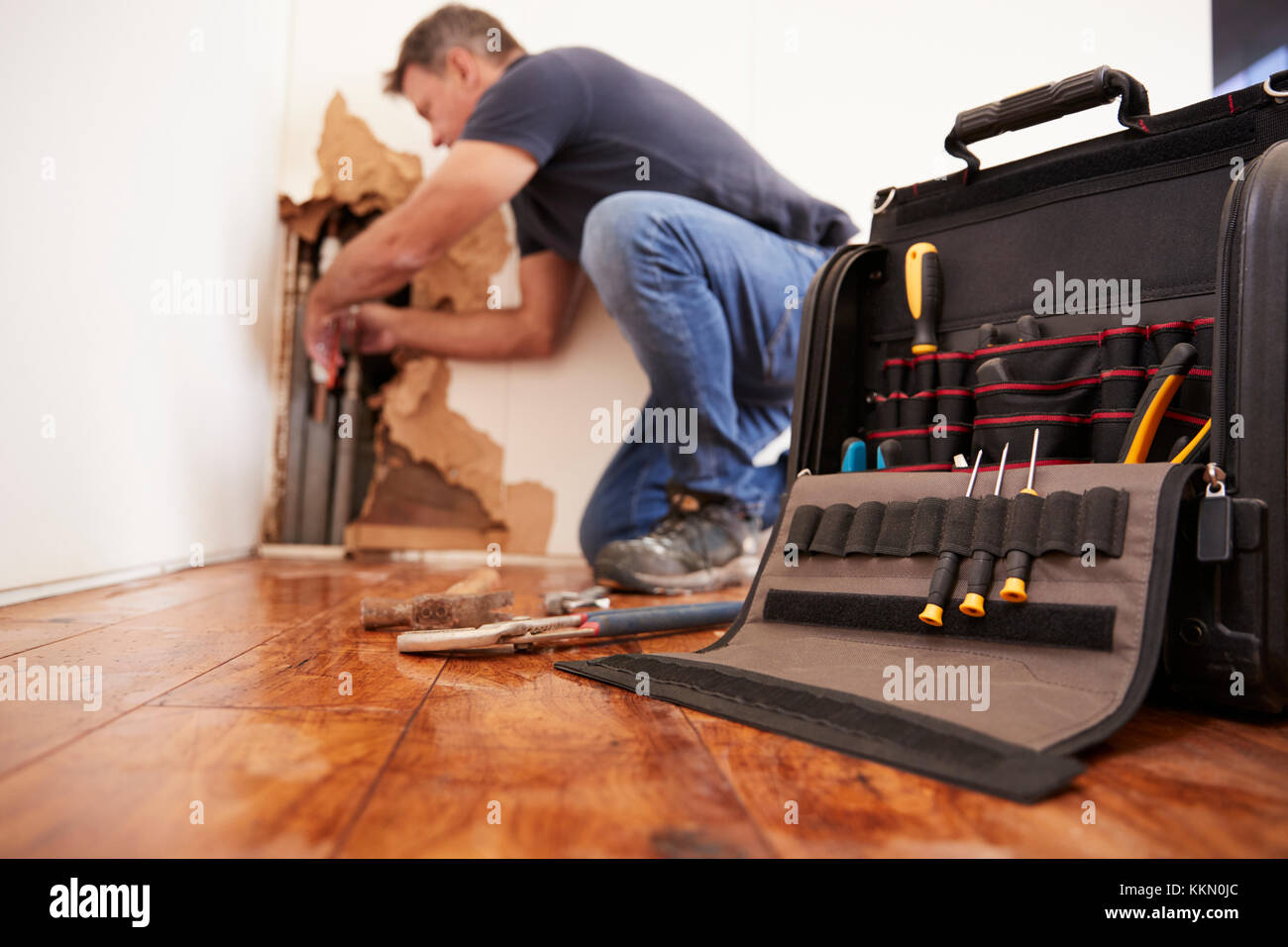 Middle aged man repairing burst pipe,plumbing, focus on foreground Stock Photo