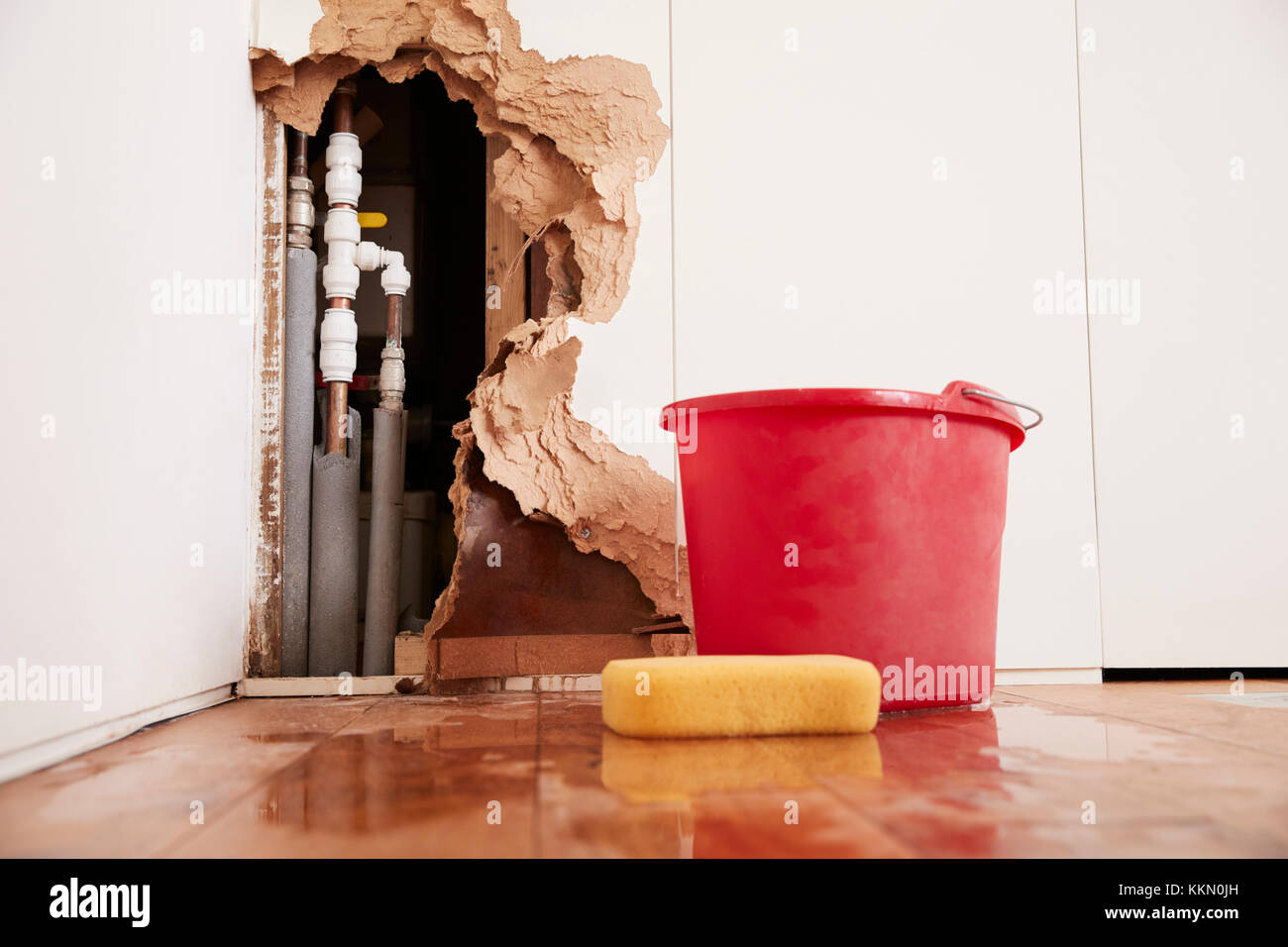 Damaged wall, exposed burst water pipes, sponge and bucket Stock Photo