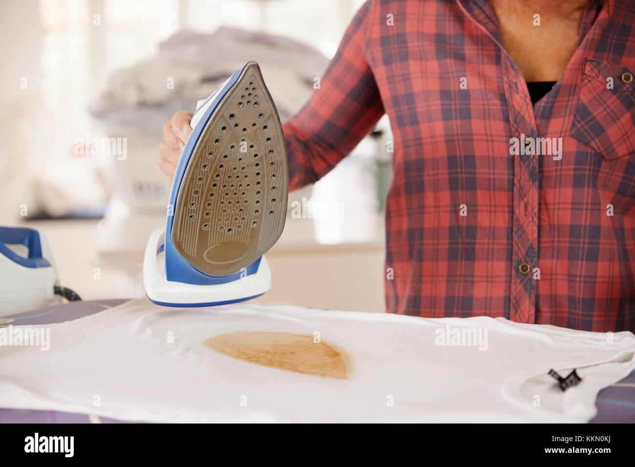 Detail of woman holding iron over burnt, damaged t shirt Stock Photo