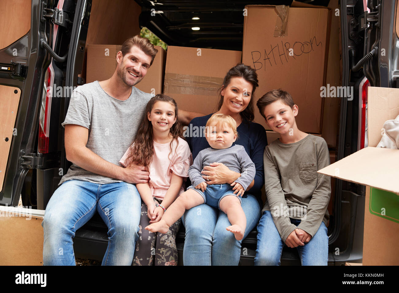 Family Sitting In Back Of Removal Truck On Moving Day Stock Photo
