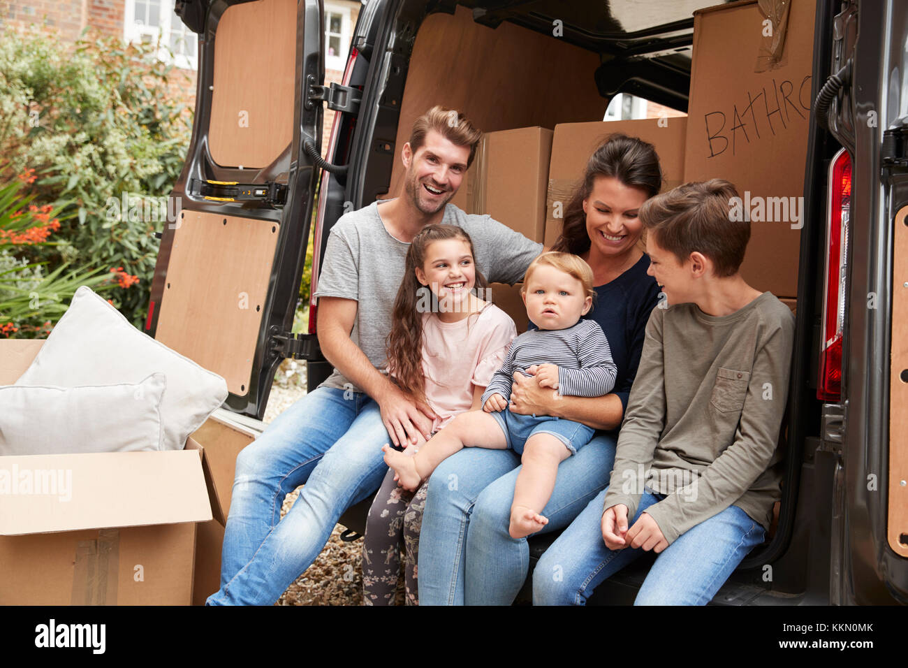 Family Sitting In Back Of Removal Truck On Moving Day Stock Photo
