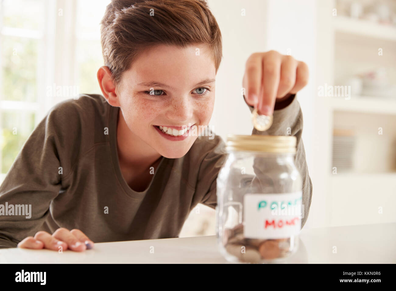 Boy Saving Pocket Money In Glass Jar At Home Stock Photo