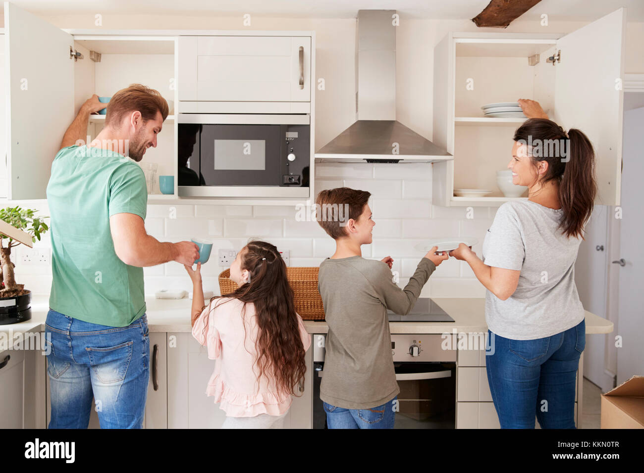 Children Helping To Put Away Crockery In Kitchen Cupboards Stock Photo