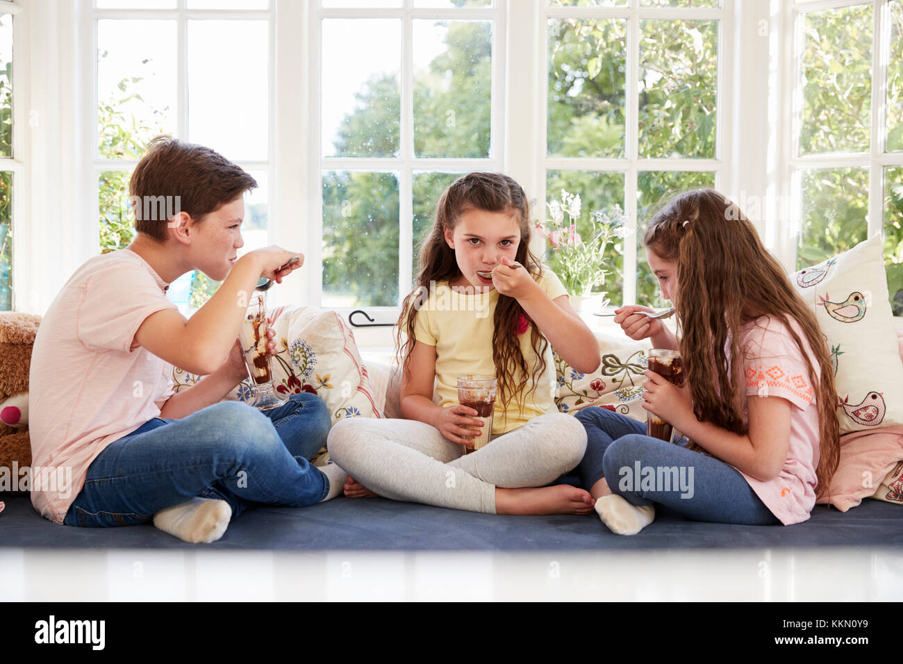 Children Sitting On Window Seat Eating Ice Cream Sundaes Stock Photo