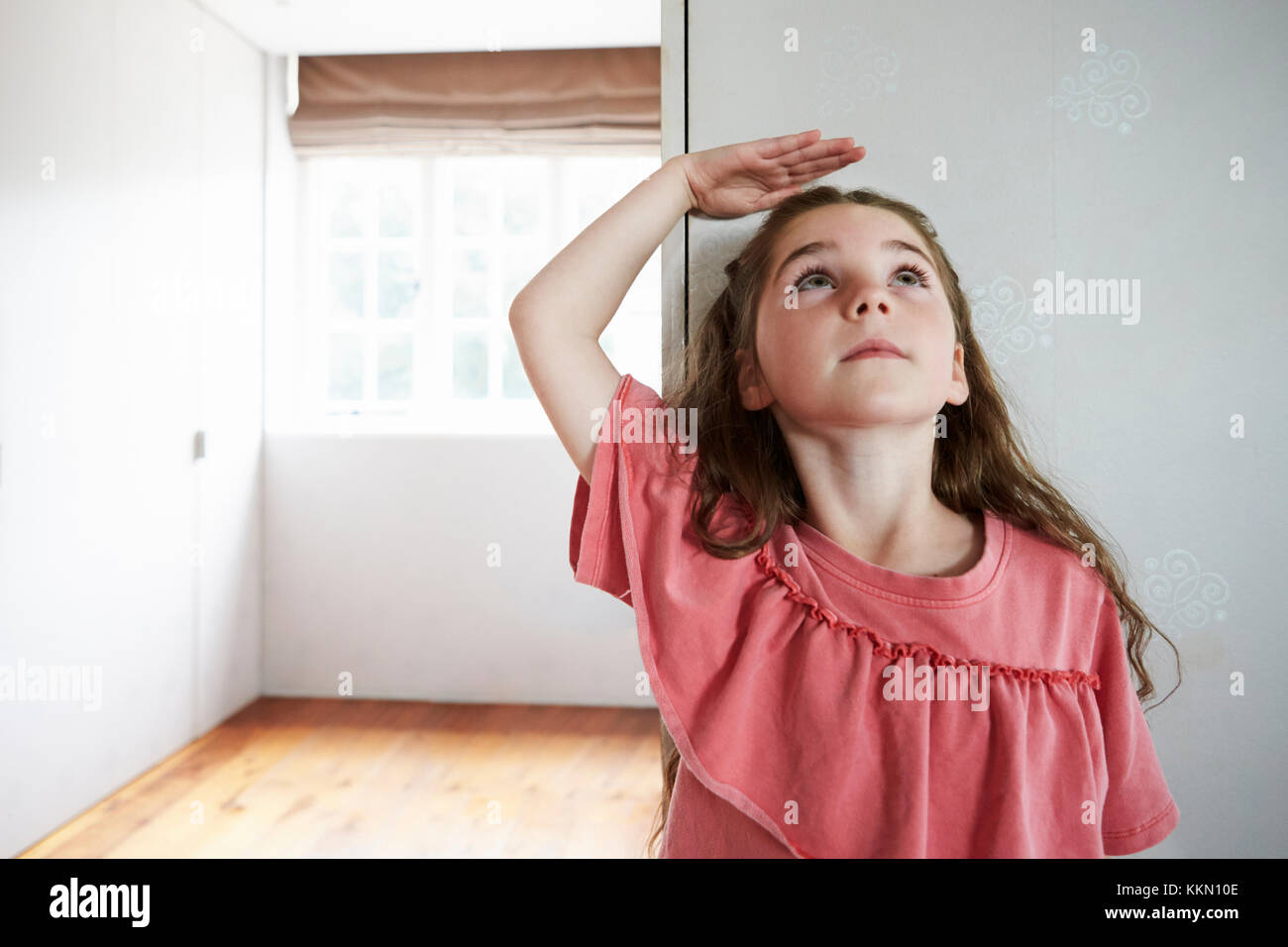 Girl Measuring Height Standing Against Wall At Home Stock Photo