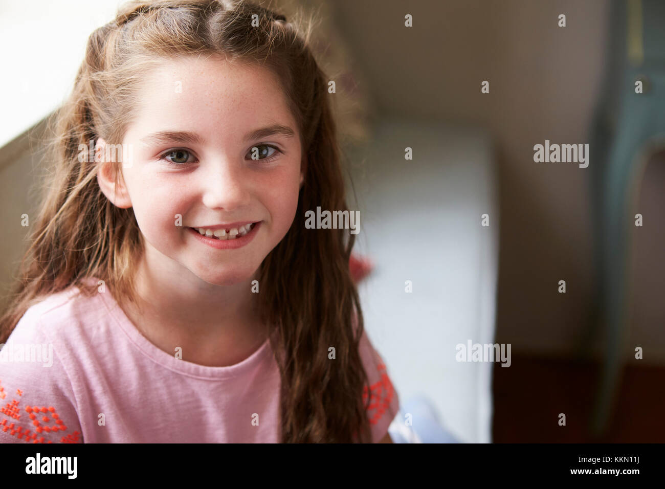 Portrait Of Smiling Young Girl Sitting On Window Seat At Home Stock Photo