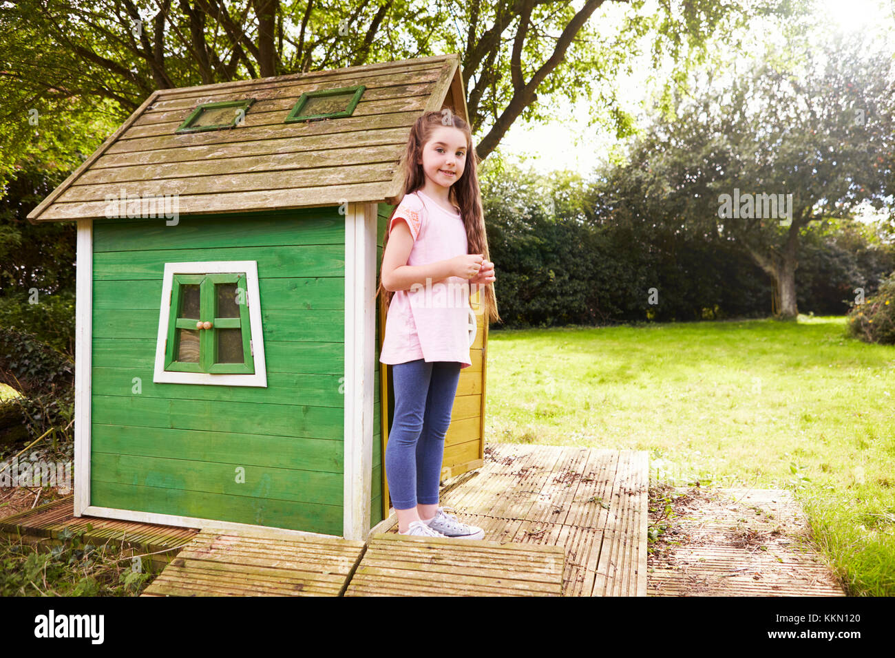 Portrait Of Girl Standing In Garden Next To Playhouse Stock Photo