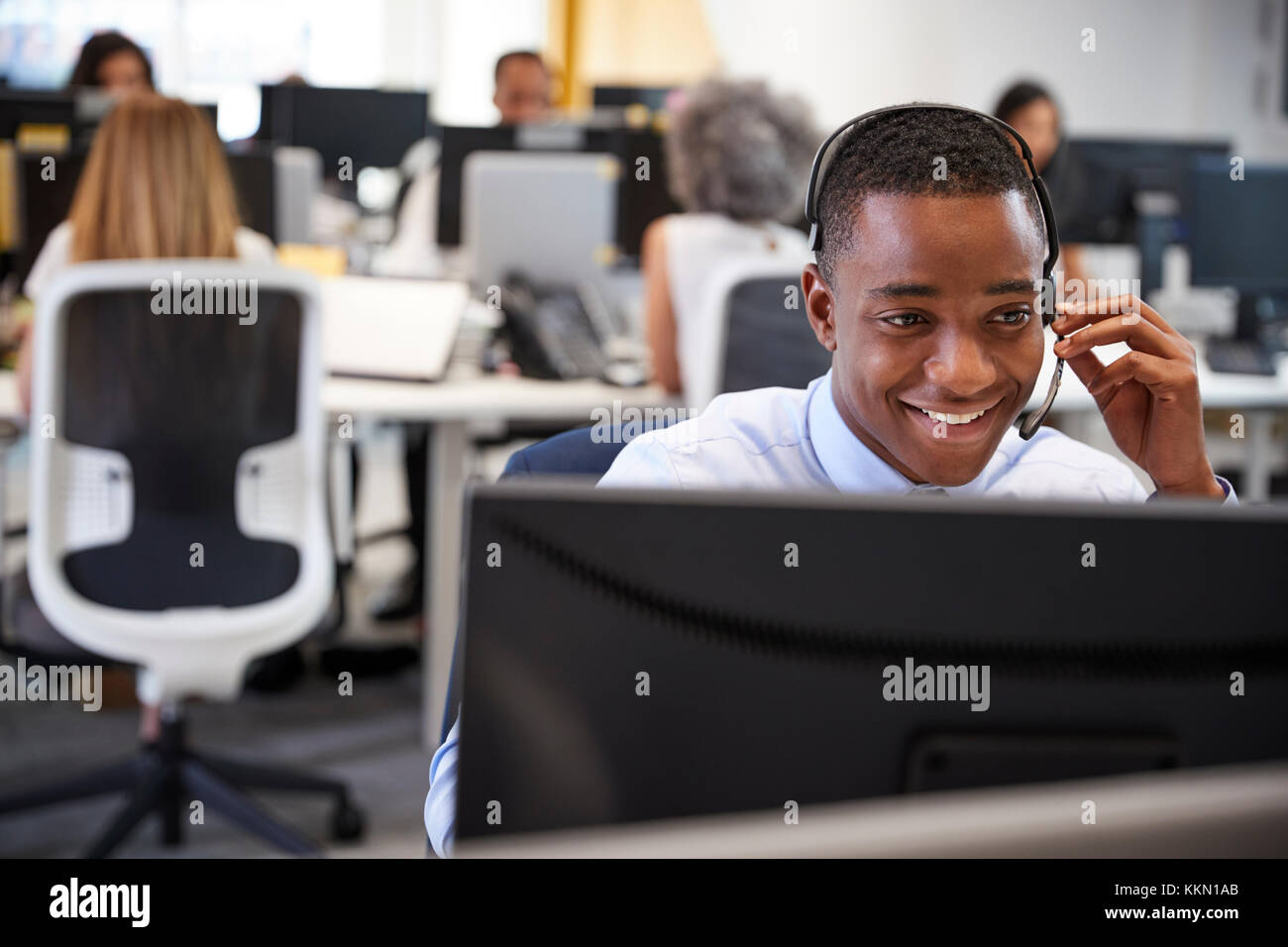 Young man working at computer with headset in busy office Stock Photo