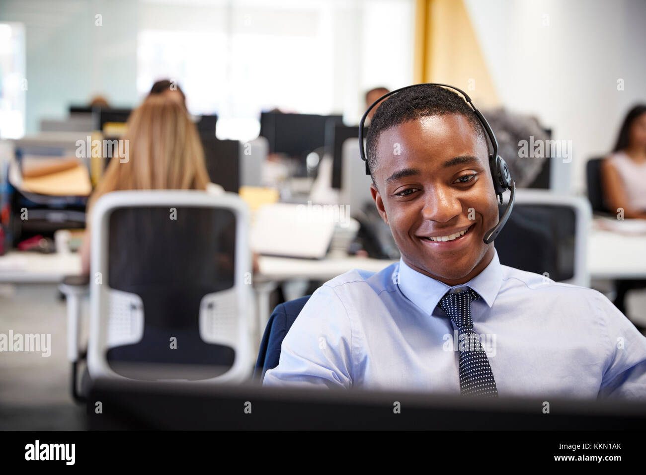 Young man working at computer with headset in busy office Stock Photo