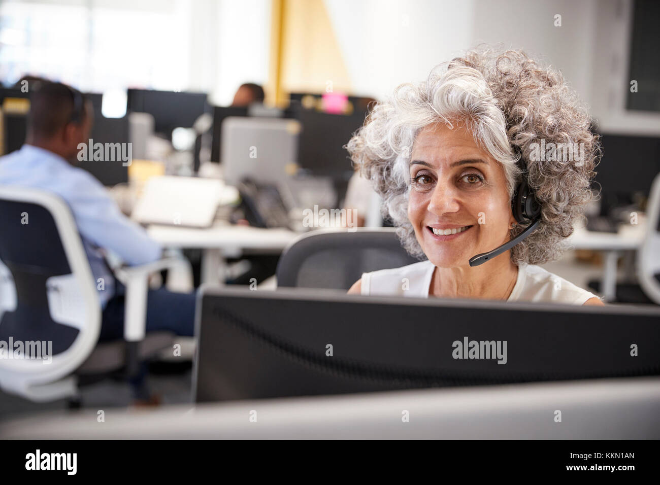 Middle aged woman working at computer with headset in office Stock Photo