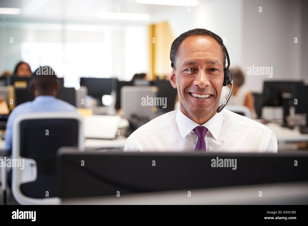 Middle aged man working at computer with headset in office Stock Photo