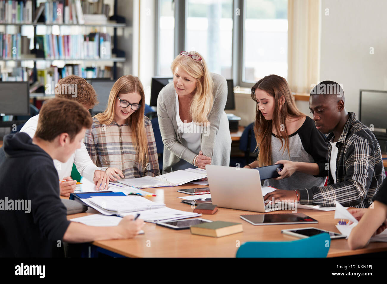 Female Teacher Working With College Students In Library Stock Photo