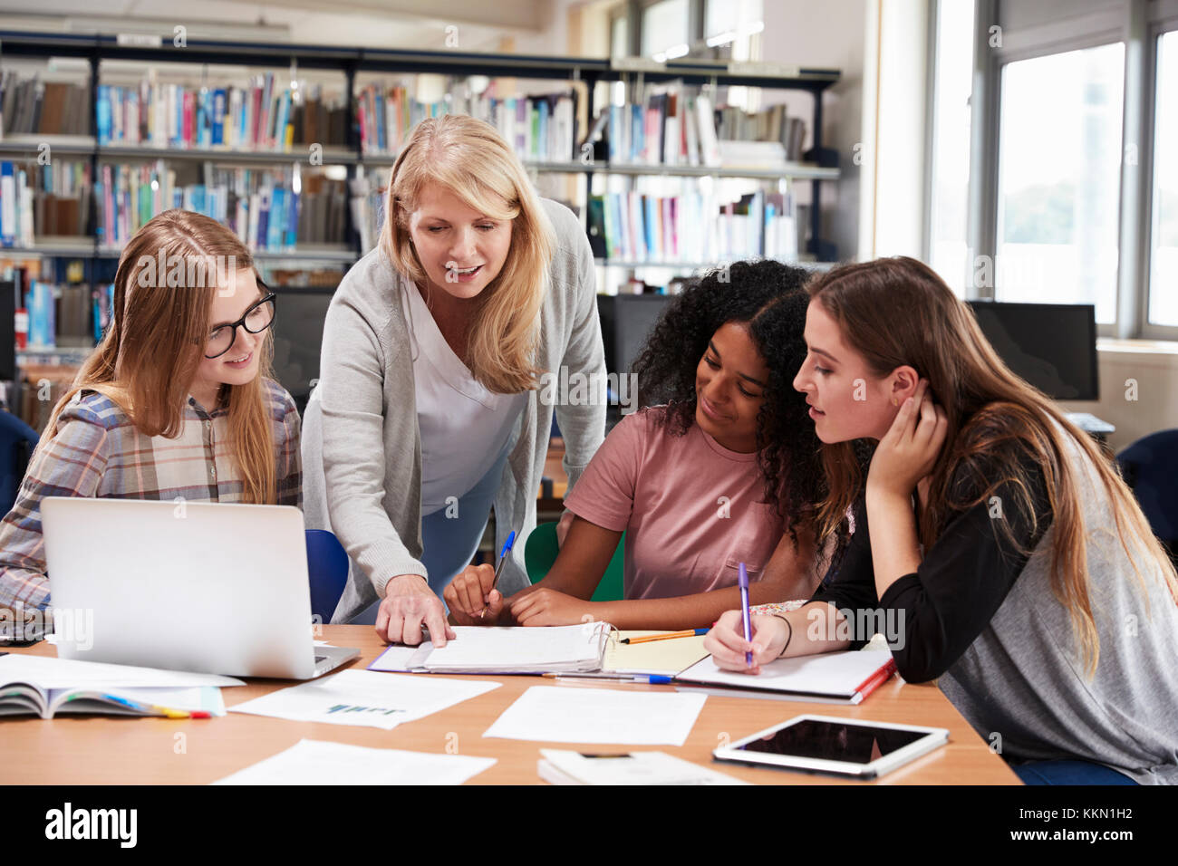 Woman Teacher Working With Female College Students In Library Stock Photo