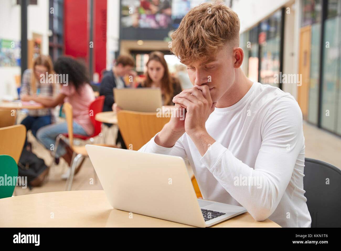 Male Student Working In Communal Area Of Busy College Campus Stock Photo