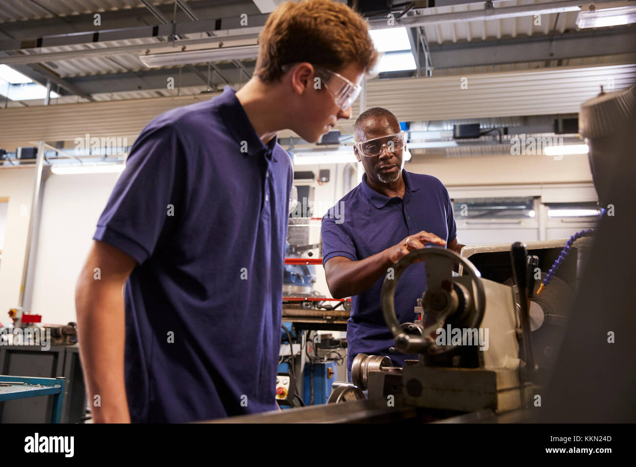 Engineer Showing Teenage Apprentice How To Use Lathe Stock Photo