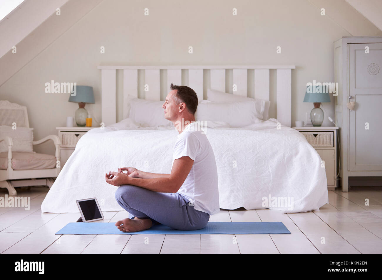 Mature Man With Digital Tablet Using Meditation App In Bedroom Stock Photo
