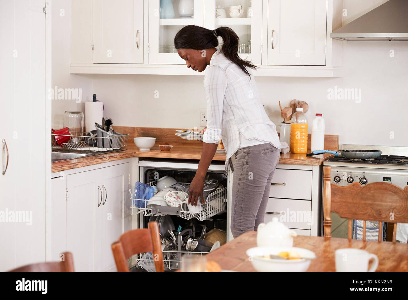 Woman Clearing Breakfast Table And Loading Dishwasher Stock Photo