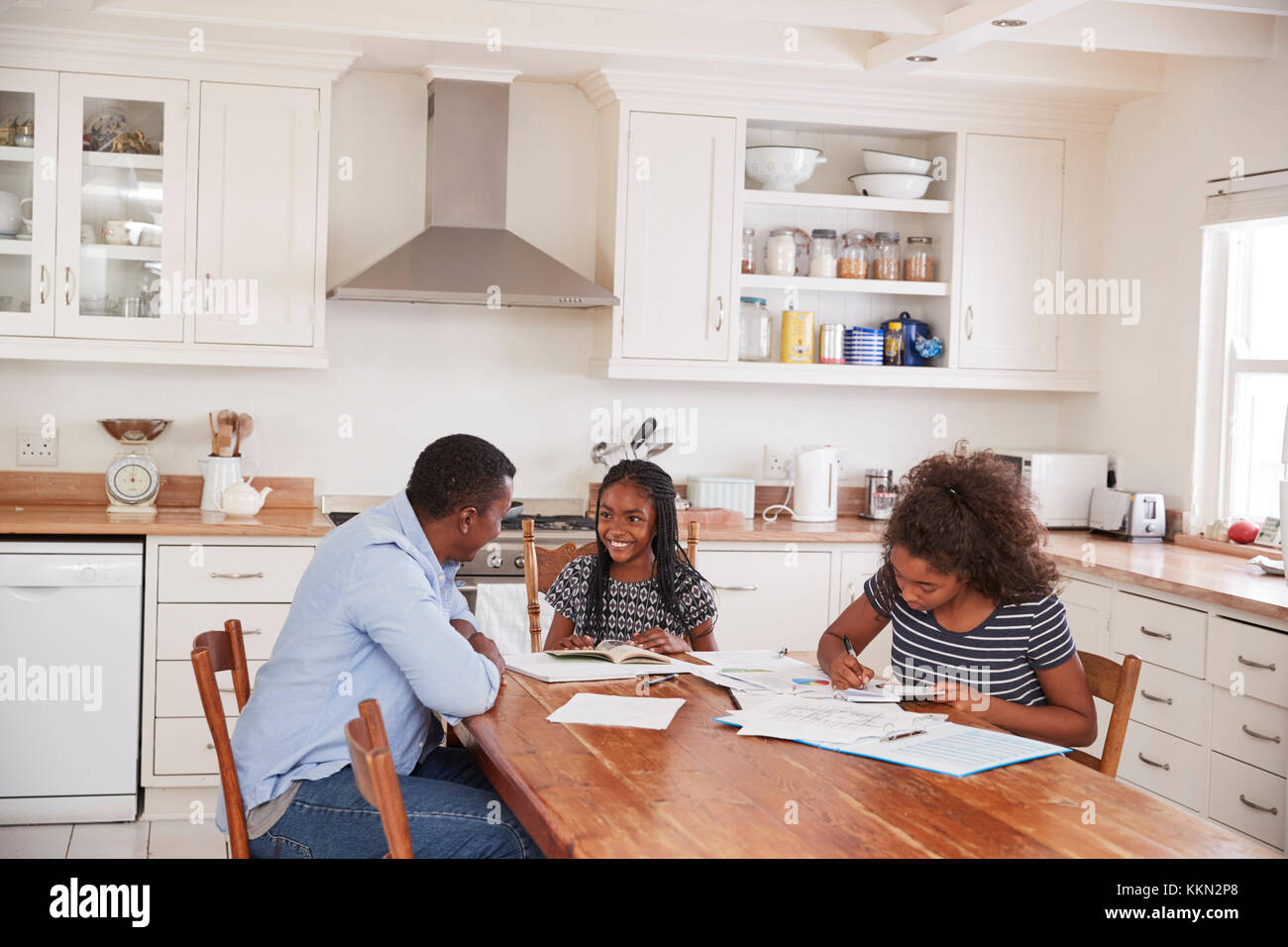 Father Helping Two Daughters Sitting At Table Doing Homework Stock ...