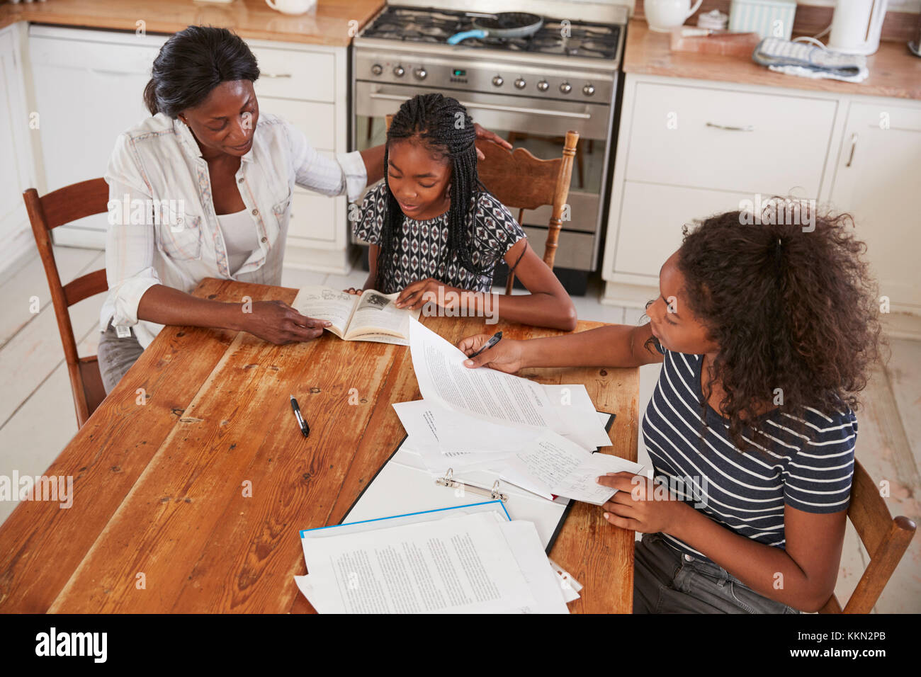 Mother Helping Two Daughters Sitting At Table Doing Homework Stock ...