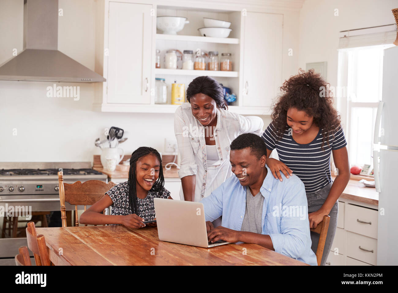 Family Around Kitchen Table Booking Vacation On Laptop Together Stock Photo