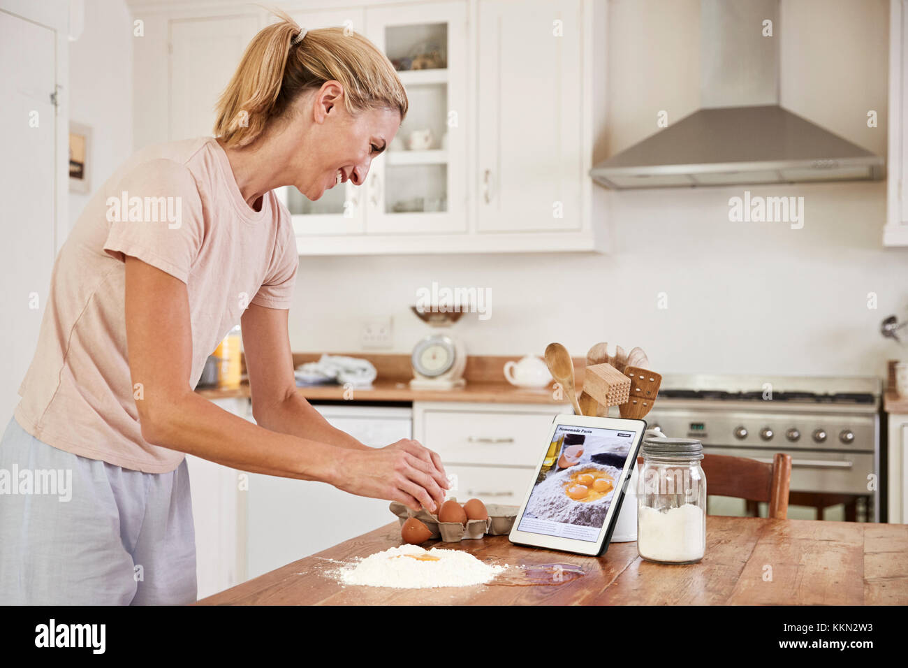 Woman Following Recipe On Digital Tablet In Kitchen Stock Photo