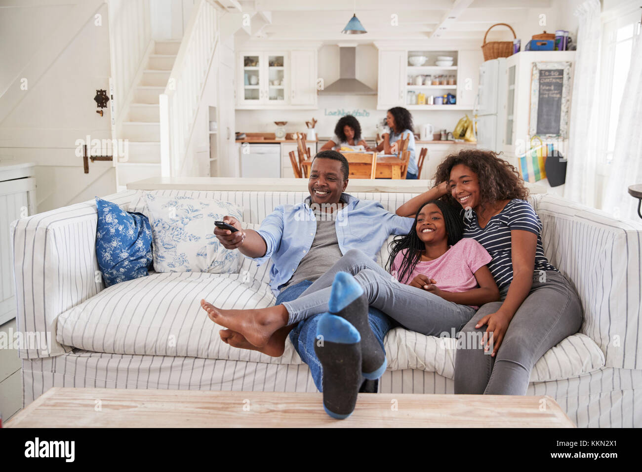 Father Sitting On Sofa Watching TV With Teenage Daughters Stock Photo