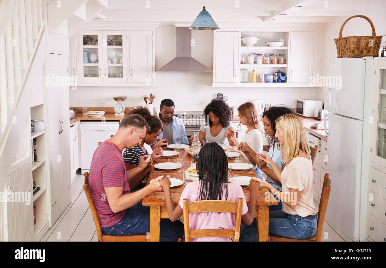 Two Families Saying Grace Before Eating Meal Together Stock Photo