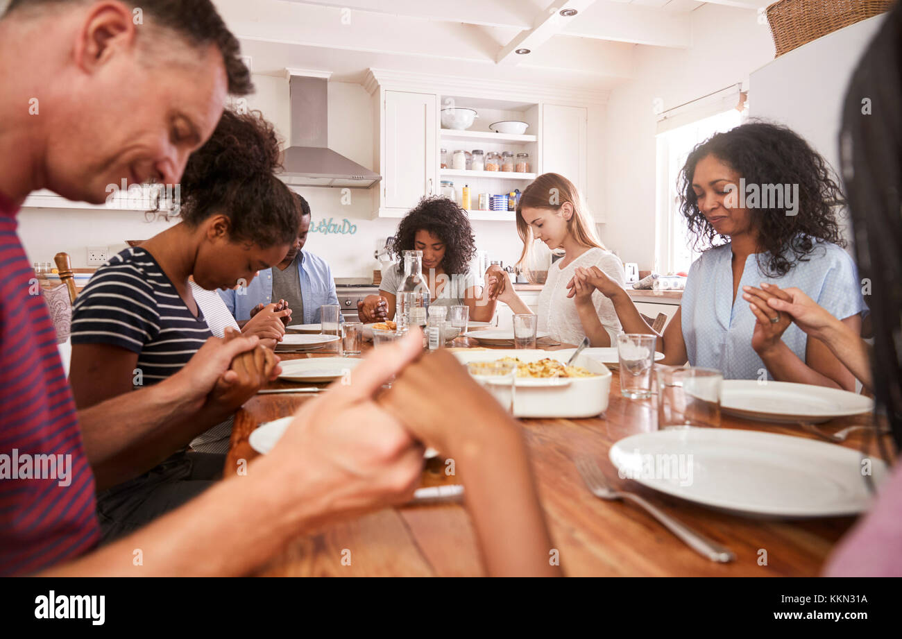 Two Families Saying Grace Before Eating Meal Together Stock Photo