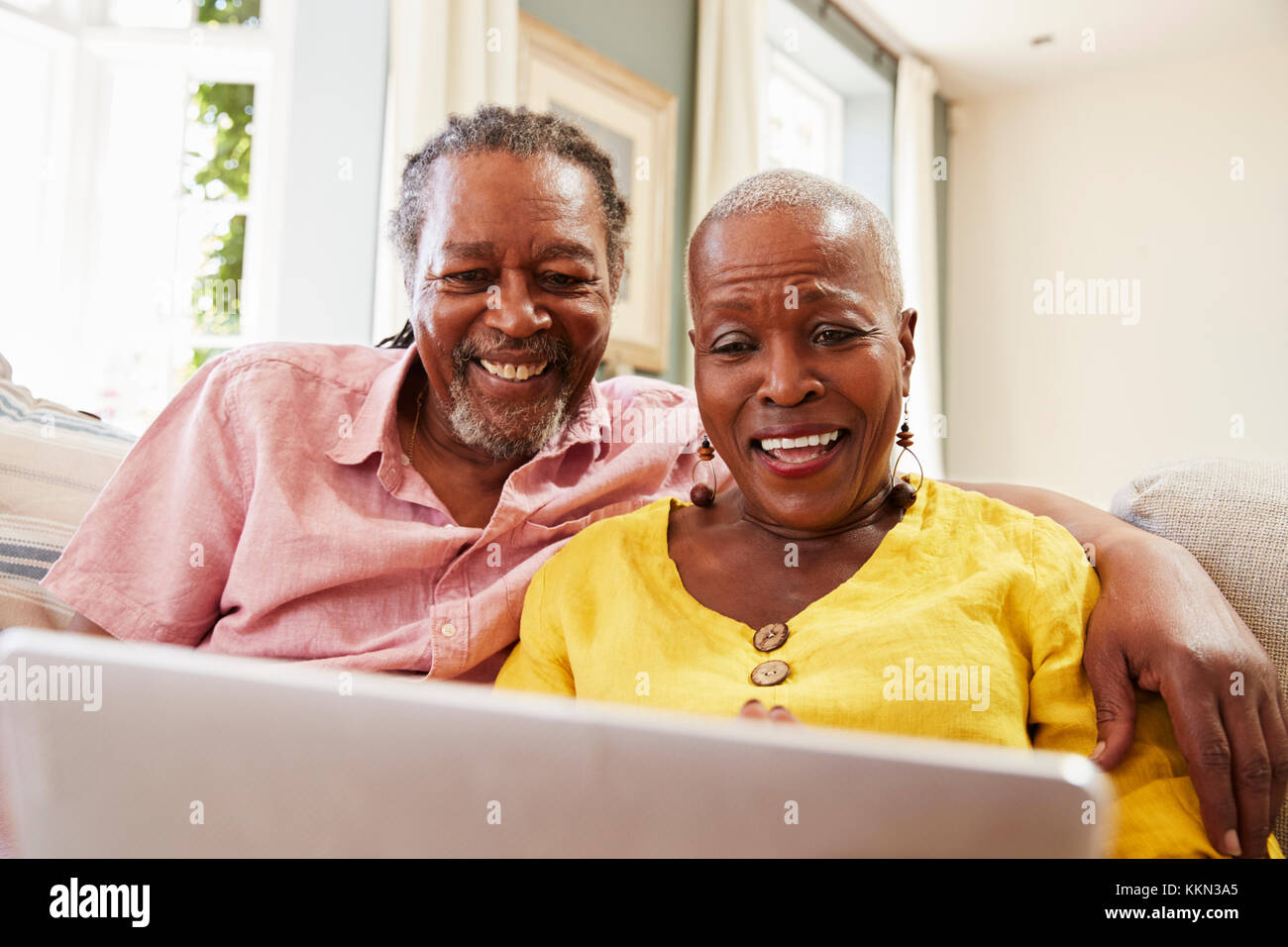 Senior Couple Sitting On Sofa Using Laptop At Home Together Stock Photo