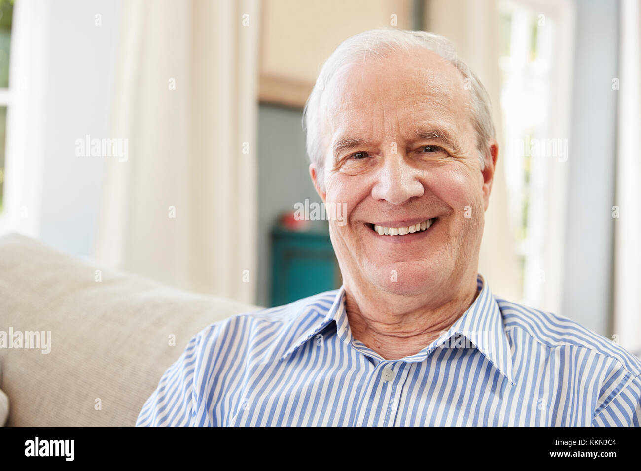 Portrait Of Smiling Senior Man Sitting On Sofa At Home Stock Photo