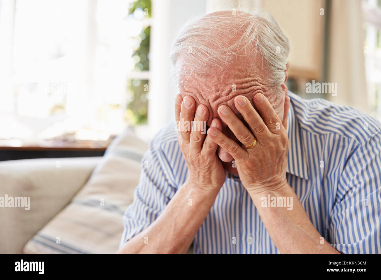 Senior Man Sitting On Sofa At Home Suffering From Depression Stock Photo