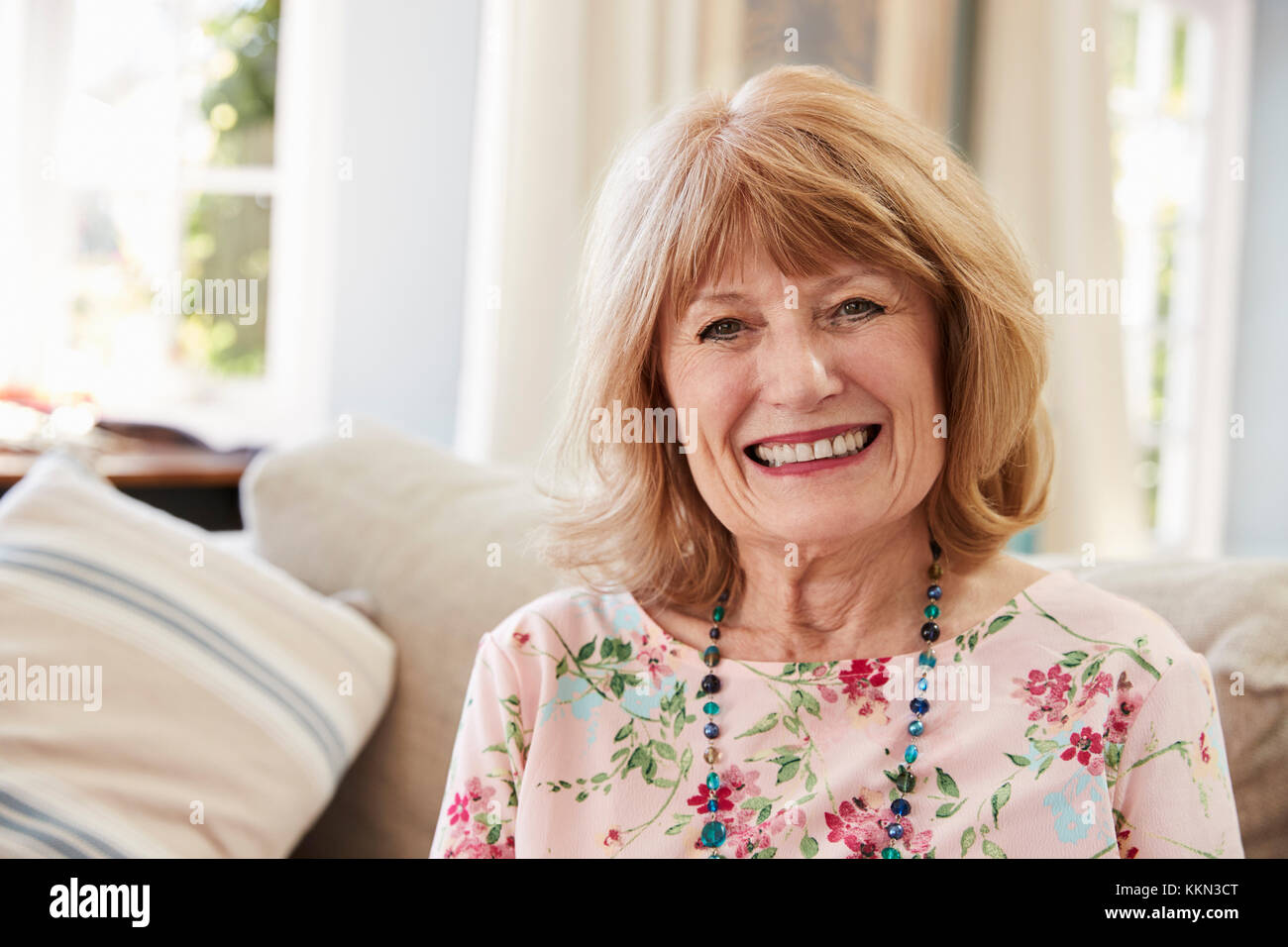 Portrait Of Smiling Senior Woman Sitting On Sofa At Home Stock Photo