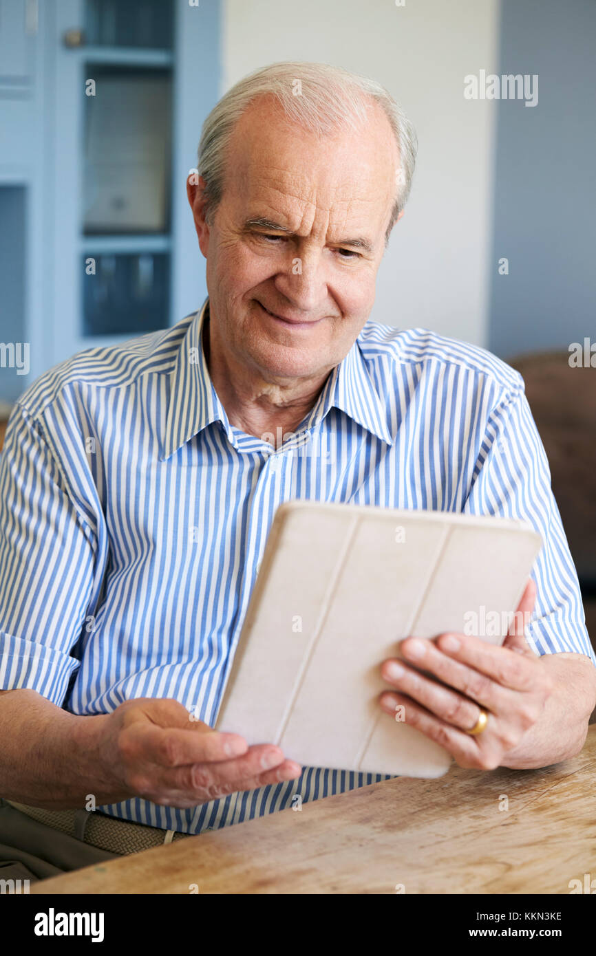 Senior Man Sitting At Home Using Digital Tablet At Table Stock Photo