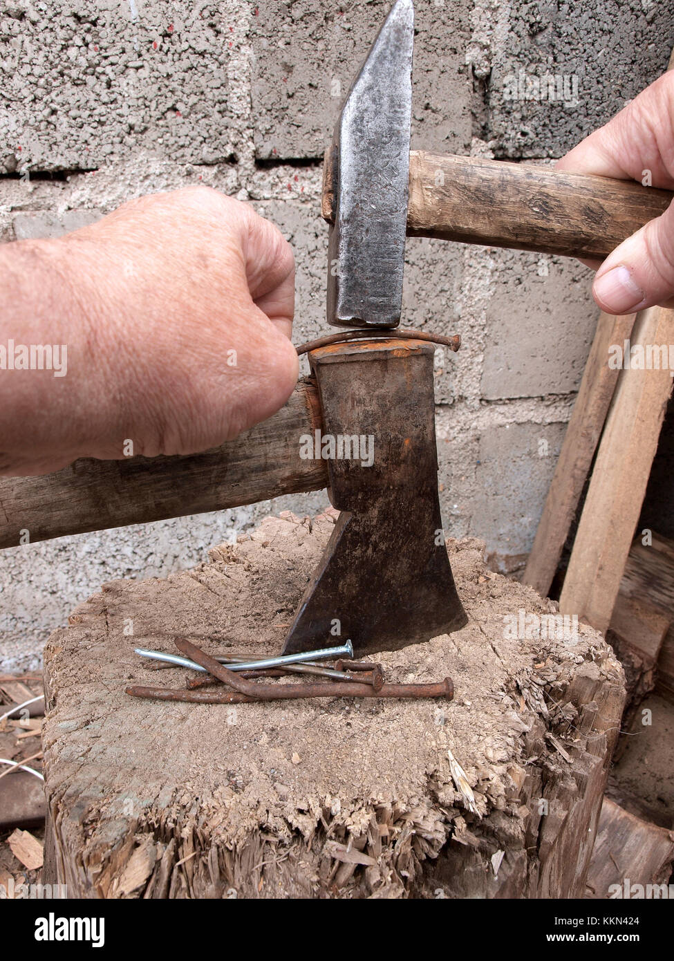 Hands straightening curved nails with hammer on old rusty axe as anvil