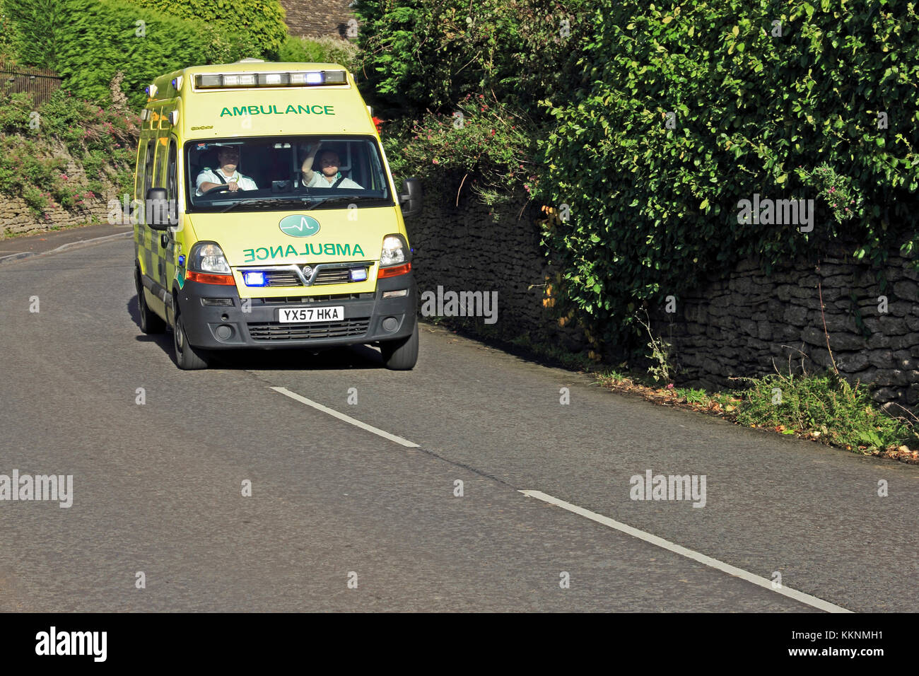 Emergency Ambulance driving down rural road with blue lights flashing Stock Photo
