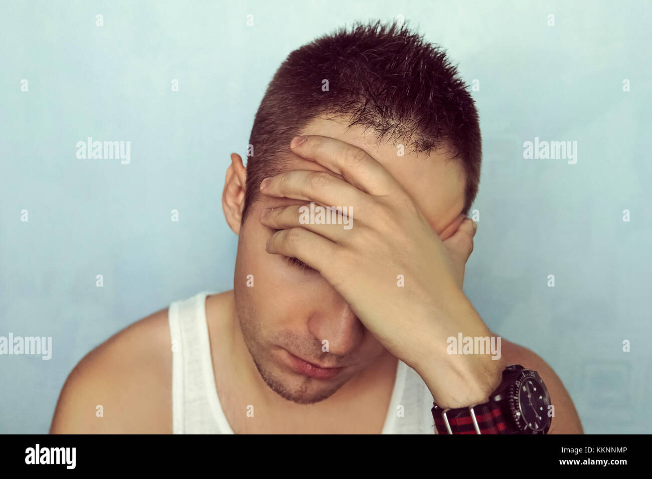 Young man squeezes his forehead, covering his face. Severe headaches or stress from hard work Stock Photo