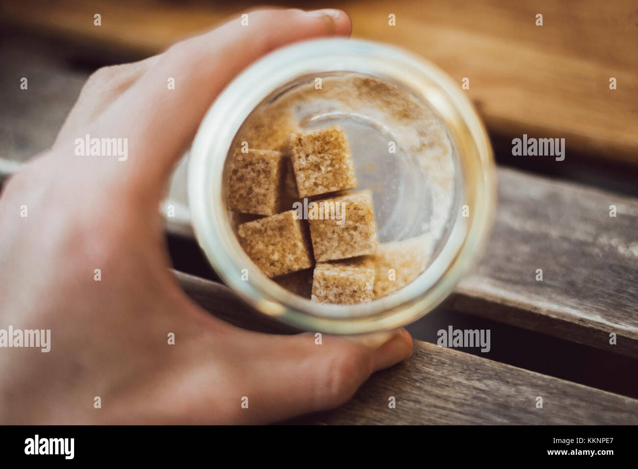 Glass with brown cubed sugar in hand on wooden table Stock Photo