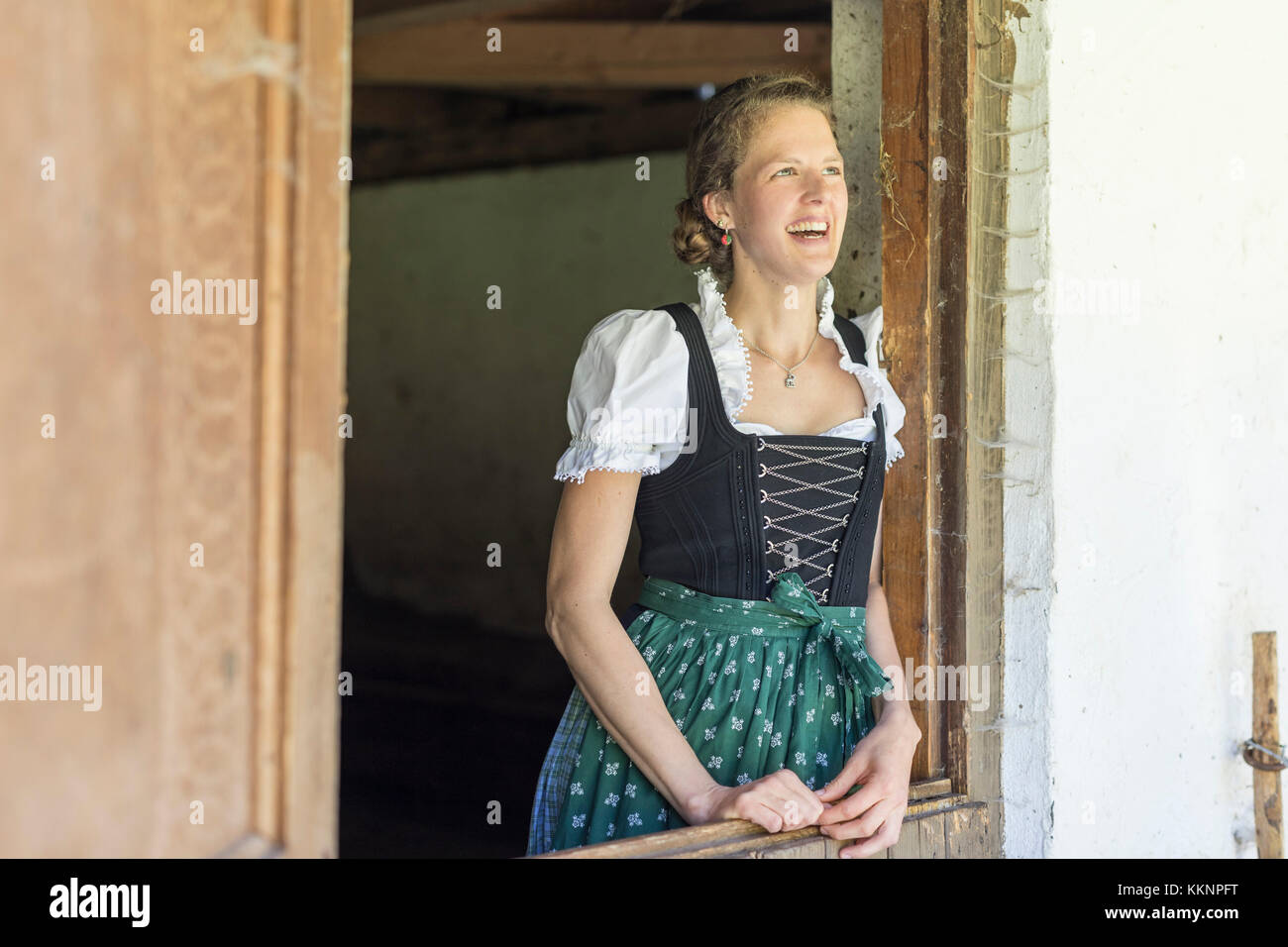 Countrywoman with dirndl looks out of a barn door Stock Photo