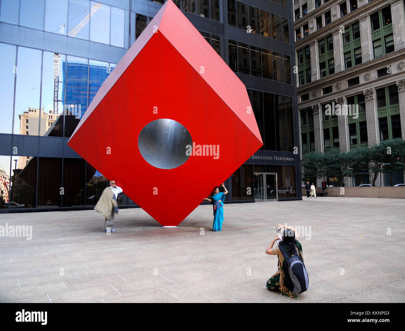 Tourists posing in front of Red Cube, a 1968 sculpture by Isamu Noguchi which sits on Broadway, between Liberty and Cedar streets in New York's financ Stock Photo