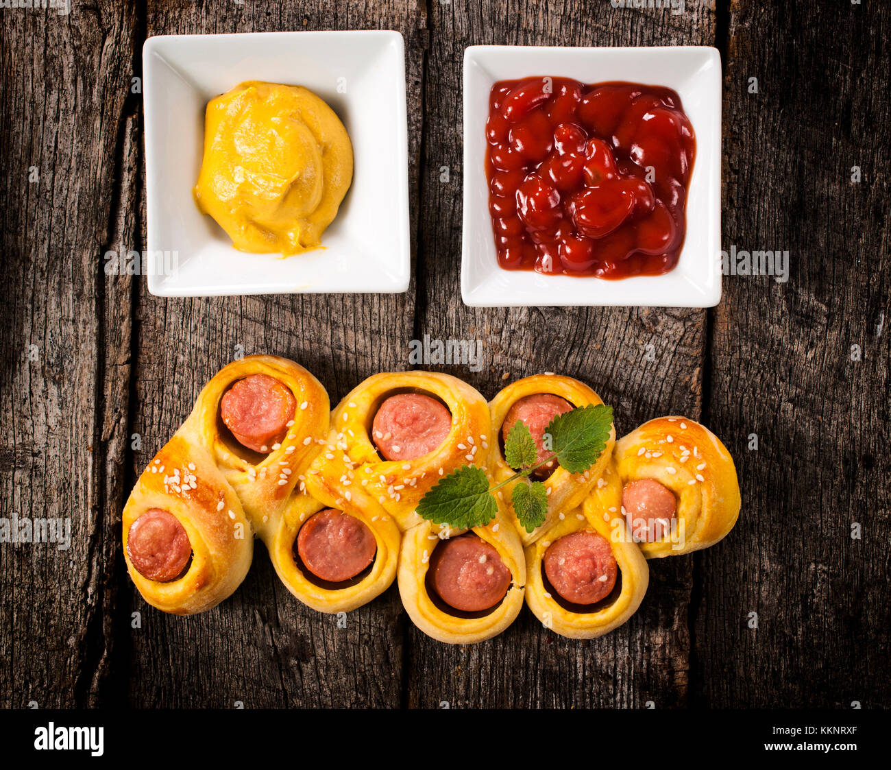 Mini hot dogs in pastry with kechup and mustard on wooden table Stock Photo