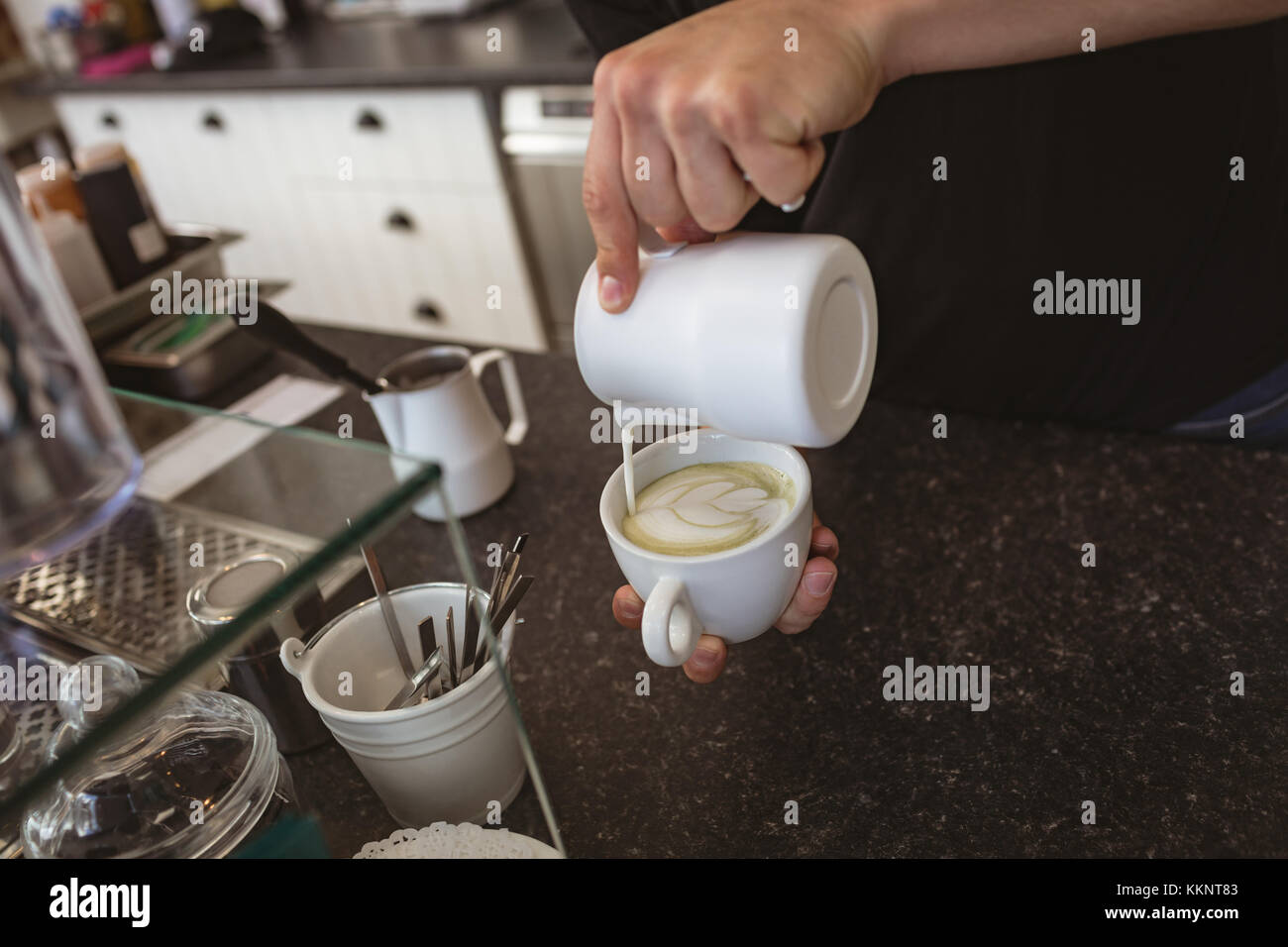 Person pouring milk into coffee mug Stock Photo