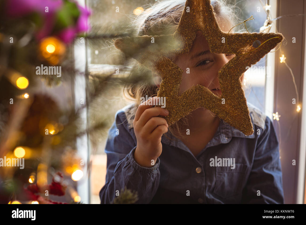 Girl looking standing near christmas tree and looking through star Stock Photo